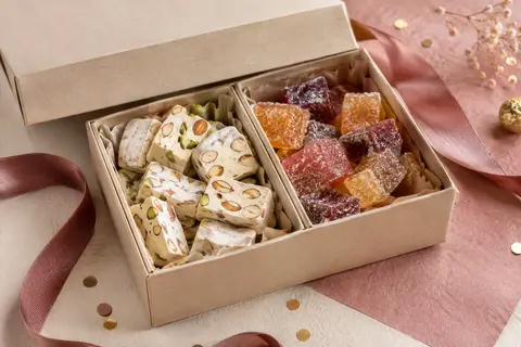 Coffret en carton avec ballotins de nougats assortis et pâtes de fruits sur un décor de fête sobre