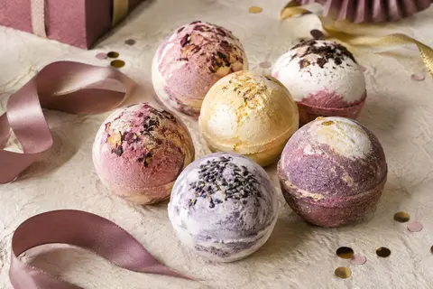 Assortiment de bombes de bain colorées posé sur un fond ivoire avec des détails festifs discrets.