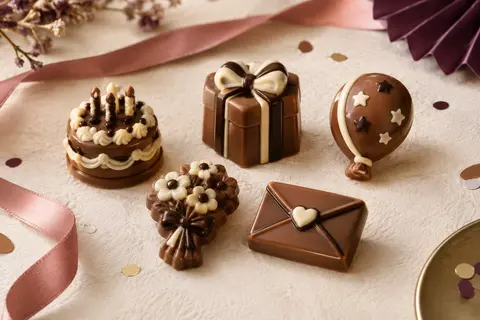 Cinq figurines d’anniversaire en chocolat au lait, décorées de détails blancs et noirs sur un fond festif