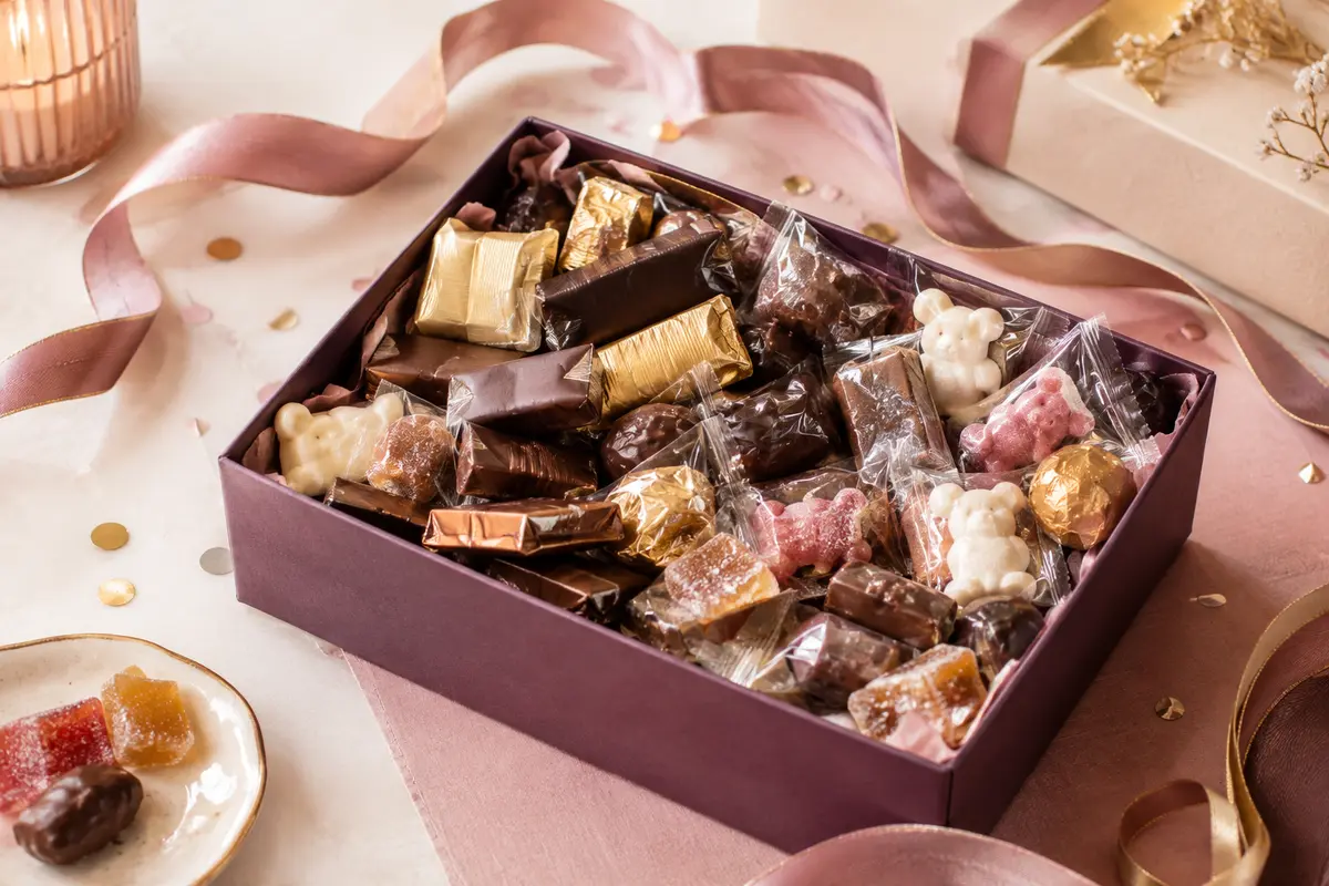 Assortiment de mini-chocolats, oursons en guimauve et pâtes de fruits présenté sur un fond de fête ivoire