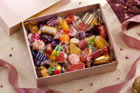 Bonbons rétro emballés individuellement, présentés sur papier ivoire avec ruban et confettis discrets.