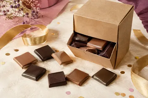 Assortiment de carrés de chocolat noir et au lait présenté dans une boîte distributrice en carton