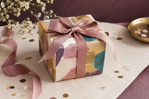 Coffret cadeau d’aventure multicolore posé sur un papier ivoire avec ruban et confettis discrets