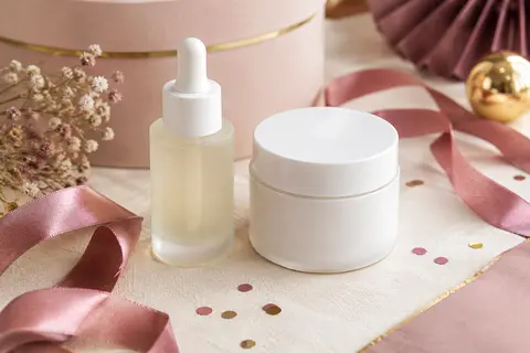 Duo de soins visage blancs, sérum et crème, présenté sur un papier ivoire avec un ruban vieux rose